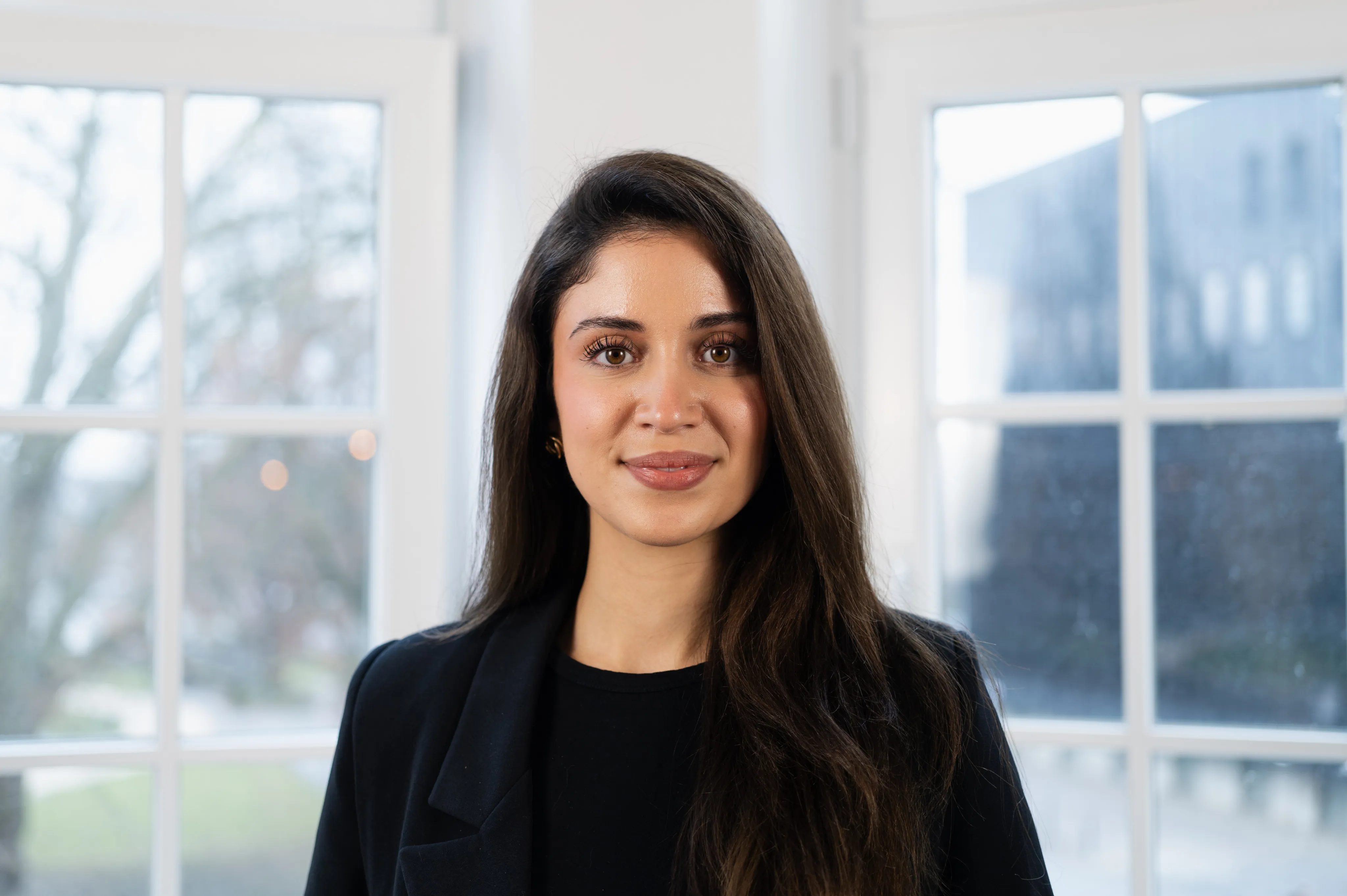 Sudenur Simsek smiles at the camera. She wears her brown hair loose and a black top.